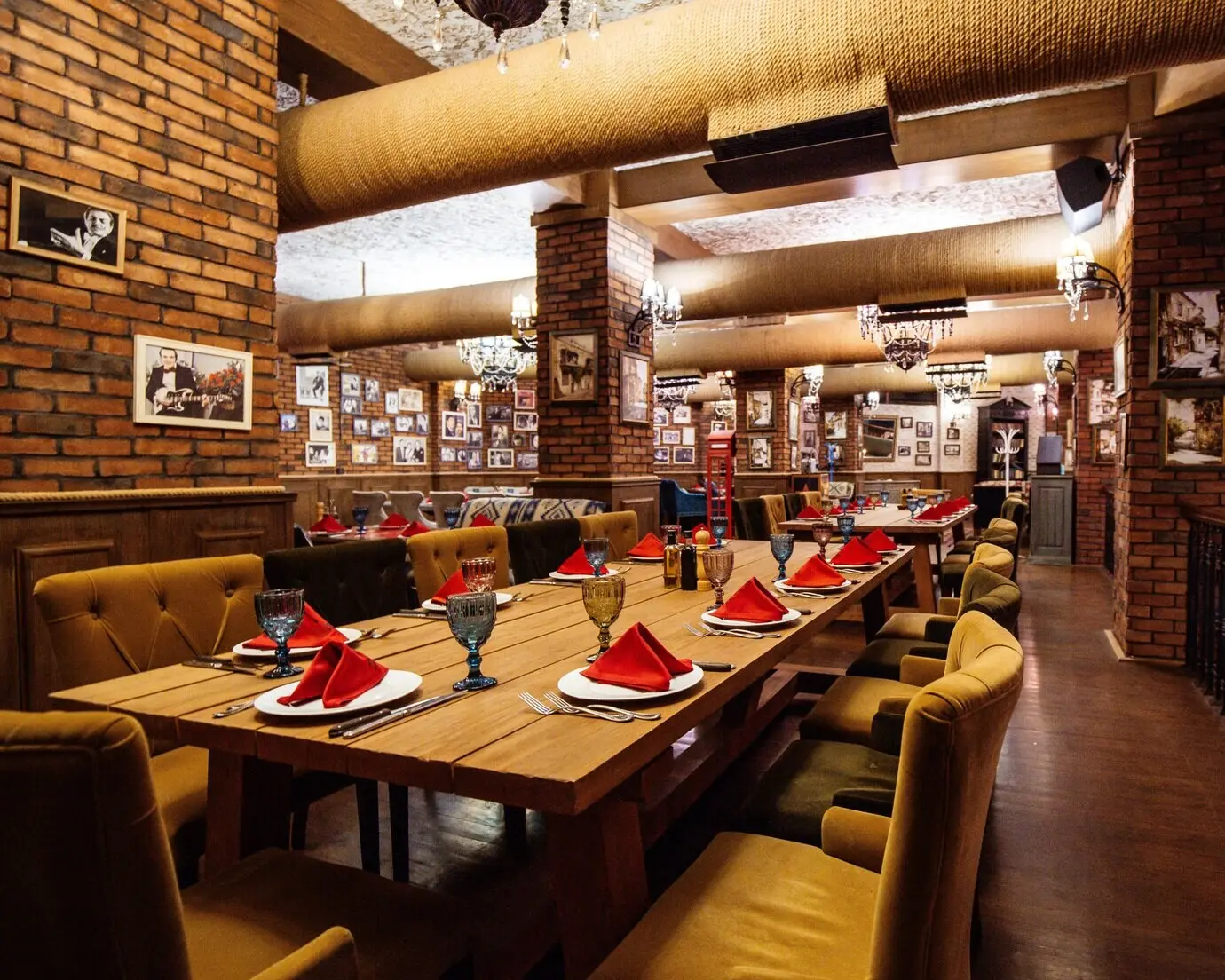 A restaurant hall featuring red brick walls, wooden tables, and pipes in the ceiling.